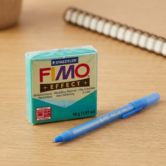 A small rectangular block of green STAEDTLER FIMO Effect modelling clay beside a blue pen and notebook.