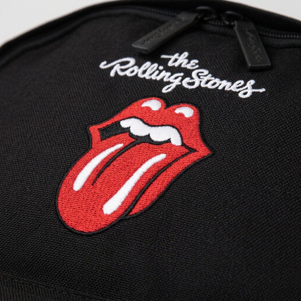 Macro close-up of the embroidered red Rolling Stones logo on black canvas, showing high-stitch detail.