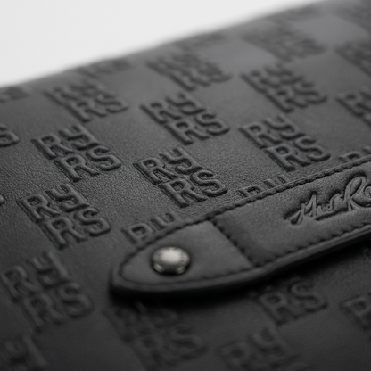 Extreme close-up of The Rolling Stones Paint It Black leather messenger bag's high-relief embossed 'RS' logo motif and signature brand plaque.