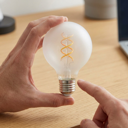 A G25 SMART+ WiFi Filament bulb held by a human hand, highlighting its true size.