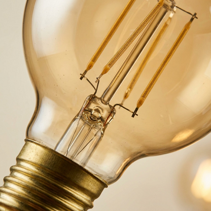 Macro detail G25 LED: visible precision-wound golden-hued filament strands, clear glass, textured brass base.