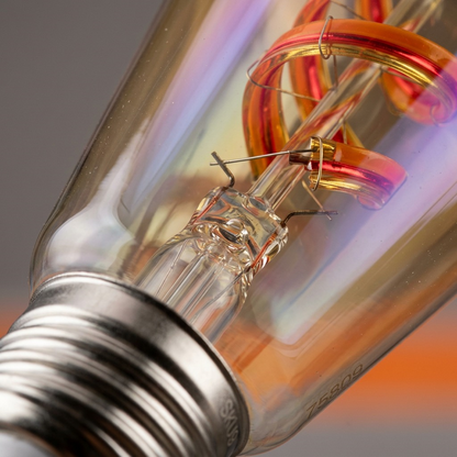 Macro detail of the LEDVANCE smart bulb, showing the colorful glass, flexible spiral filament, and metal base.