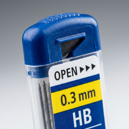 An extreme close-up detail shot of the top of the STAEDTLER lead tube, showing the blue cap grip texture, the integrated opening tool, and very clear text details for 0.3 mm and HB.