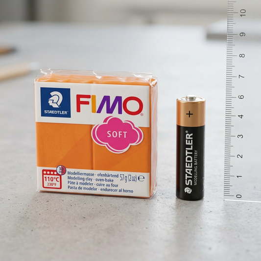 A photo-realistic scale reference image showing the Fimo Soft tangerine modelling clay next to a standard AA battery.