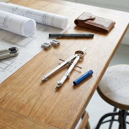 A lifestyle image showing the Staedtler Mars Limited bow compass and blue lead canister on a wooden drawing board.