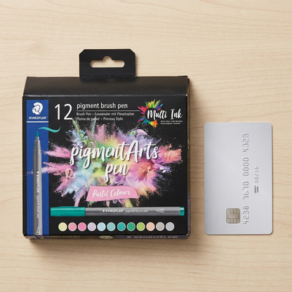 A scale reference image showing the STAEDTLER set beside a standard credit card on a wooden desk.