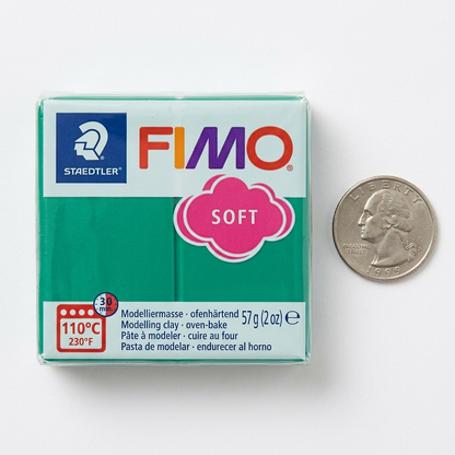 A scale-reference image showing the STAEDTLER Fimo Soft Emerald oven-bake clay block, with its green body, red-orange header, FIMO and STAEDTLER logos, and 'SOFT' scallop, positioned alongside a common US Quarter coin.
