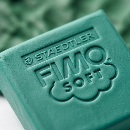 Macro extreme close-up of emerald green Fimo Soft clay texture, showing clear embossed text and details.