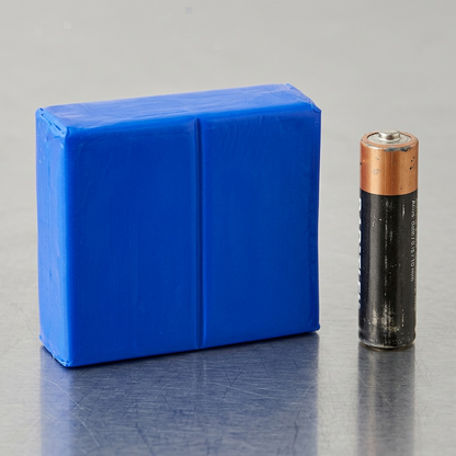 A block of STAEDTLER Fimo Soft Brilliant Blue clay next to a standard AA-size battery for size comparison.