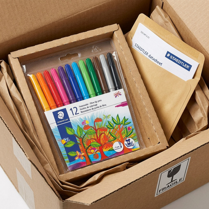 A photographic scene showing the STAEDTLER water-based markers in their plastic case, securely nestled inside a protective cardboard box filled with paper padding.