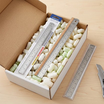 A realistic photo of multiple packaged STAEDTLER rulers and one being unboxed from a cardboard box.