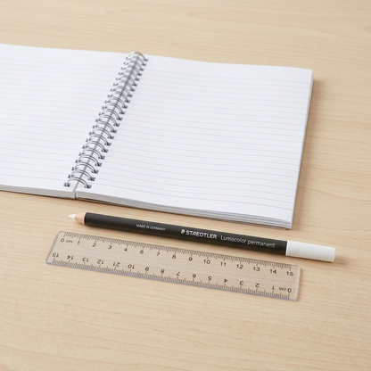 A photograph of the STAEDTLER white marker on a desk next to an open notebook and ruler.