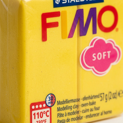 A close-up photograph showcasing the texture and multi-layered branding of an unwrapped block of yellow Fimo Soft modeling clay.