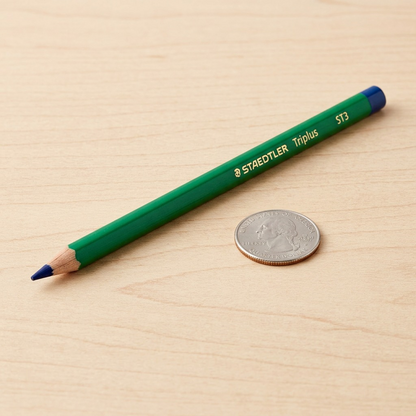 A close-up shot of a single STAEDTLER Triplus watercolor pencil resting alongside a standard USD quarter.