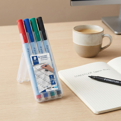 A photo of the Staedtler marker set prop-up case next to an open notebook and coffee mug.