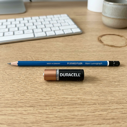 A scale reference shot, showing the specific blue Staedtler Mars Lumograph pencil beside a standard AA battery.