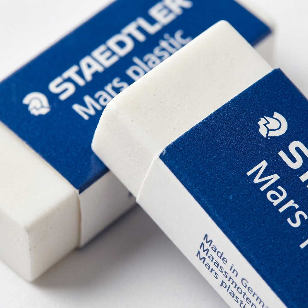 A macro photo of two white STAEDTLER Mars plastic erasers, showing the fine text and textured sleeves.