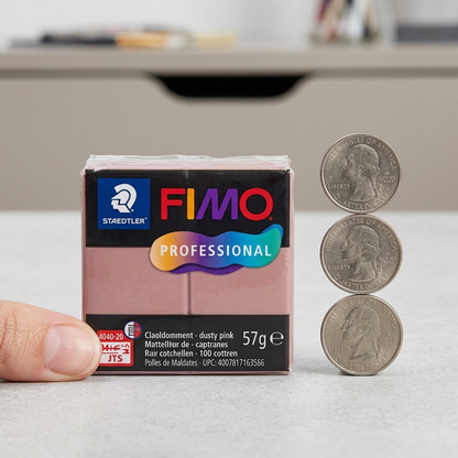 A photograph showing the STAEDTLER Fimo Professional Dusty Pink 57g block next to a standard AA battery. The block is in its exact retail packaging. Both objects rest on a white surface, demonstrating the small size of the clay.
