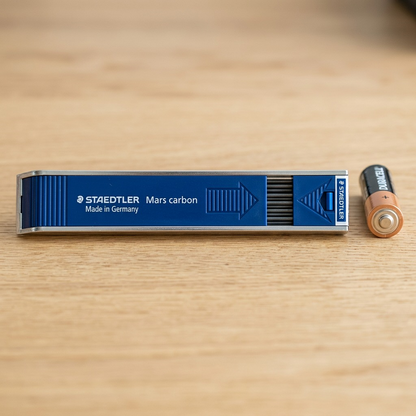 An image showing the STAEDTLER Mars Carbon lead dispenser placed next to a standard AA battery for scale reference.