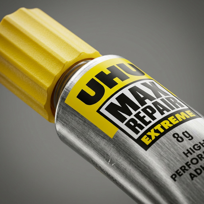 An extreme close-up photograph focusing on the textured surface of the UHU Max Repair Extreme metal tube and yellow plastic cap.