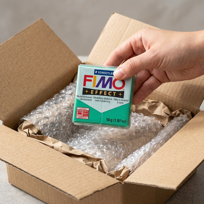 A close-up unboxing shows a Staedtler Fimo Effect Green clay block safely in protective bubble wrap.