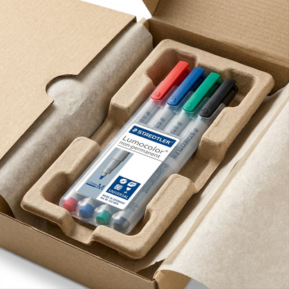 Premium-feel close-up photograph of the STAEDTLER Lumocolor M set in protective cardboard shipping inside a larger box.