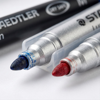 A macro photo of two STAEDTLER permanent marker tips showing blue and red medium-sized felt nibs.