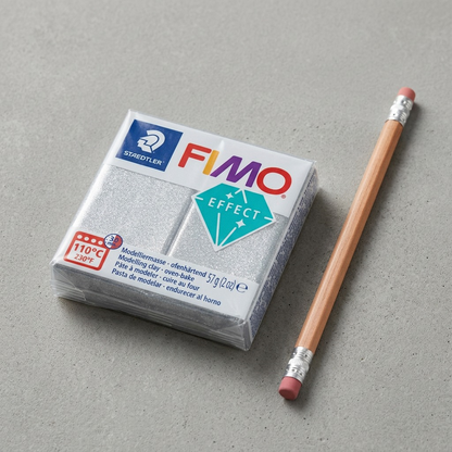 A single package of FIMO Effect Silver Glitter clay is placed beside a standard wooden pencil, clearly demonstrating its compact size.