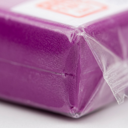 An extreme close-up of the textured, rich purpure-colored Fimo Soft clay through its transparent wrap, with soft lighting and a shallow depth of field.