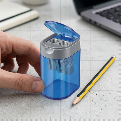 A Staedtler blue oblong tub sharpener sits next to a classic wooden pencil on a textured light desk.