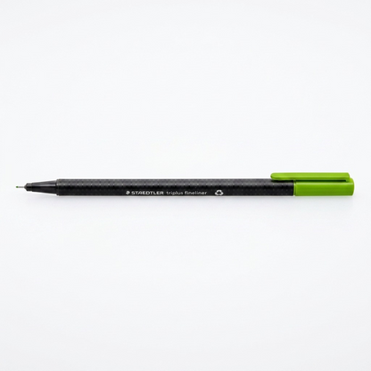 A crisp, central product shot of the STAEDTLER triplus fineliner (green) on white, featuring its unique hexagonal body and metal-clad tip.