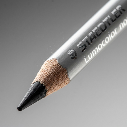 A macro photo of the Staedtler non-permanent pencil showing sharp wood grain, matte black lead, and clear silver printing.