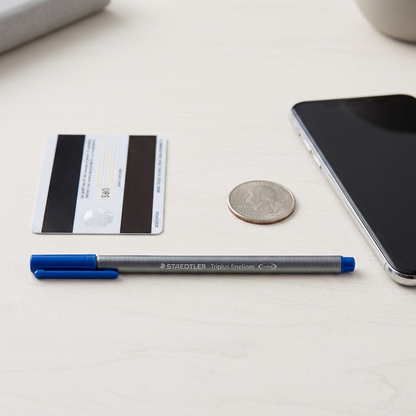 An overhead photo comparing the STAEDTLER Triplus 334-3-A7 fineliner to an ID card and USB drive.