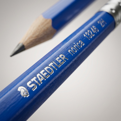Macro detail of the STAEDTLER Norica 2H pencil showing the precise silver foil printing on the blue barrel.