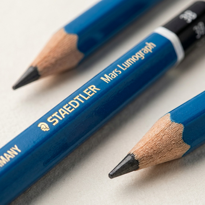 A macro photograph focuses sharply on the high-quality gold STAEDTLER print, showing texture on the blue lacquer and the defined "3B" grade. The black dip with its silver ring is visible at the very top.