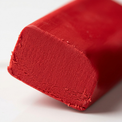 A macro photograph focuses on the edge of the unwrapped red modelling clay, showing a detailed cross-section of its smooth texture.