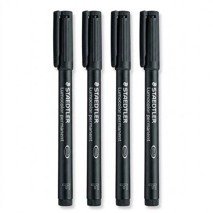 High-resolution macro photograph of four black Staedtler Lumocolor permanent markers, upright on a white background.