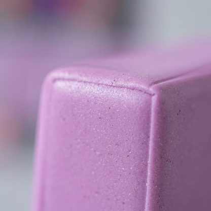 An extreme macro close-up reveals the dense, fine-grained surface texture of the Lavender STAEDTLER FIMO Professional clay, showing subtle pigment particles and a smooth matte finish, with a blurred lavender background and premium lighting.
