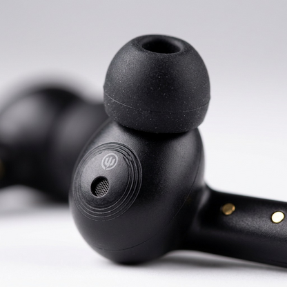 Macro image of black Wicked Audio Mojo 500 earbud showing ear tip, logo, grille, and gold charging contacts.