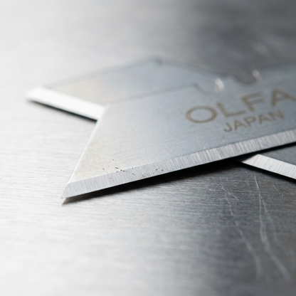 Macro shot focuses on the honed double edge of a single SKB-2 safety blade, with light catching the metal.