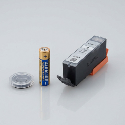 An image showing the Canon PGI-9 Clear Ink Tank sitting next to a standard AA battery.