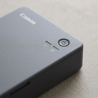 Macro view of the Canon SELPHY QX20's textured gray finish, power button, and indicator icons.